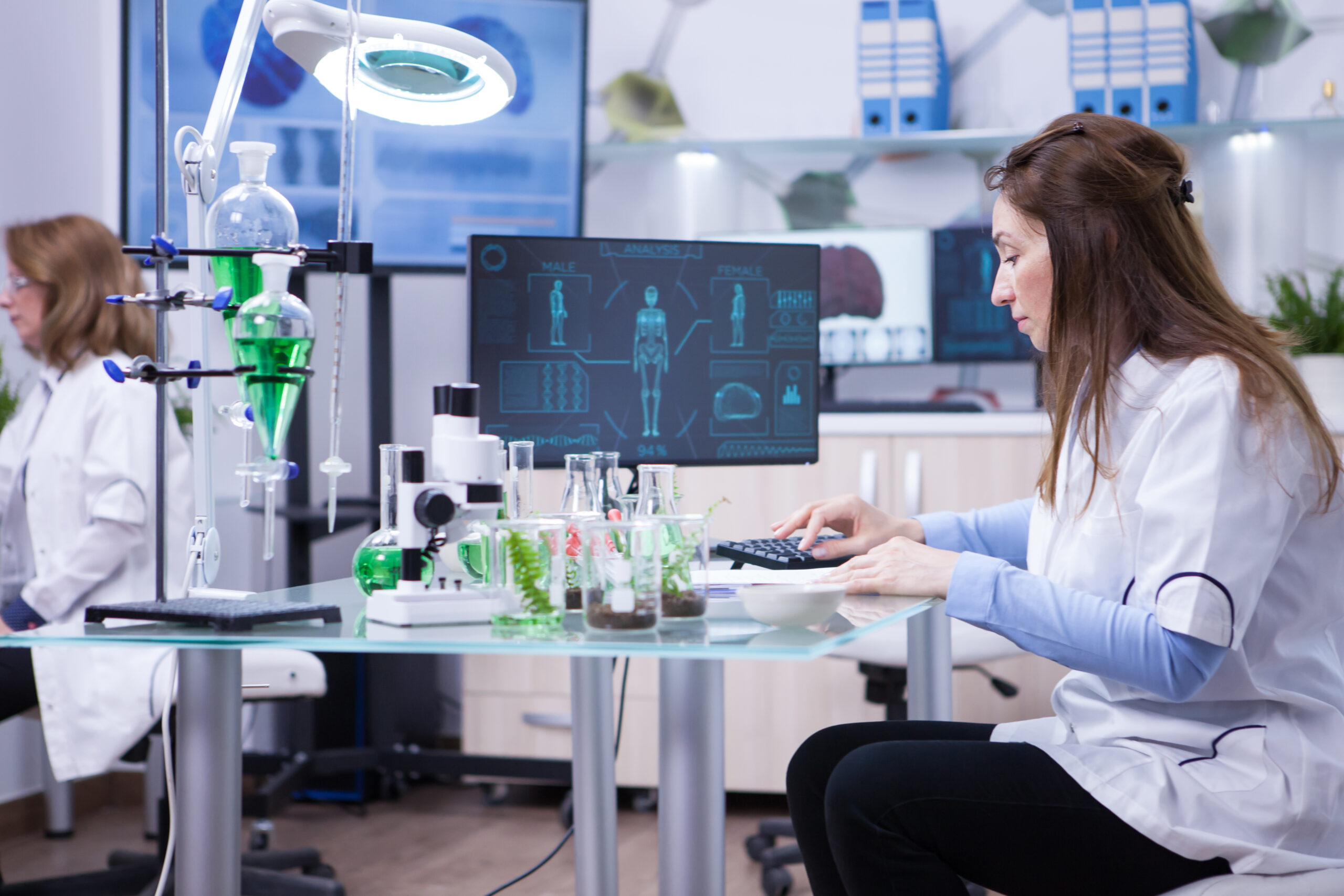 Female scientist typing on her computer the data from last scientific tests. Chemistry lab.